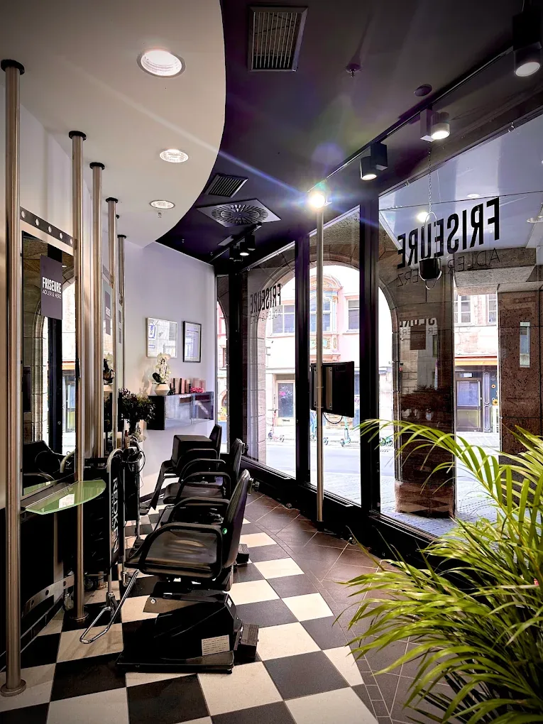 Friseursalon Adler & Herz mit schwarz-weißem Schachbrettboden, schwarzen Frisierstühlen an der Spiegelwand und Fensterfront zur Straße